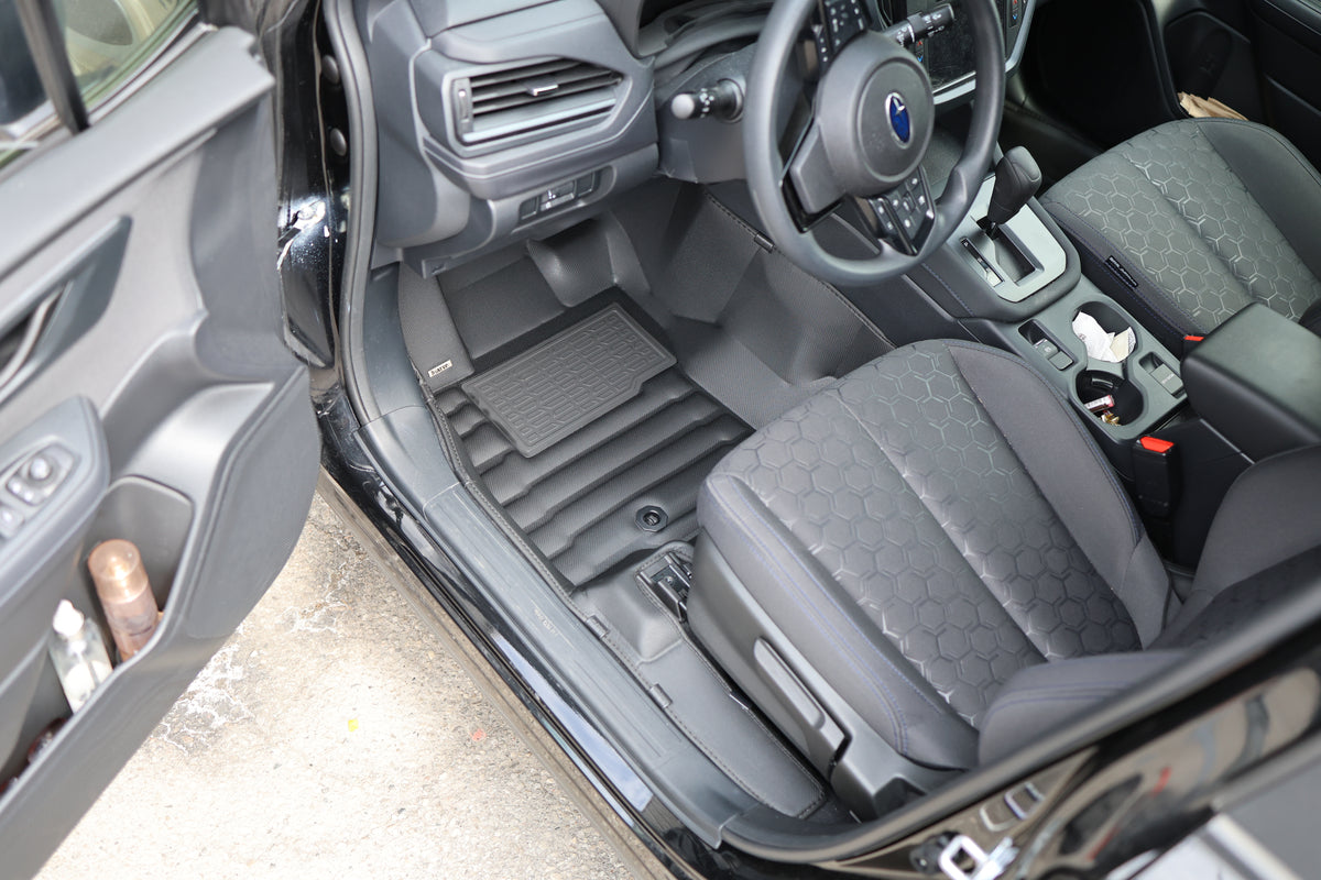 Driver footwell of a Genesis with tan leather seats and a black Mat Up! mat running under the pedals and up to the sill